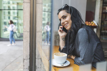 Lächelnde Frau, die in einem Café sitzt und telefoniert - WPEF01803