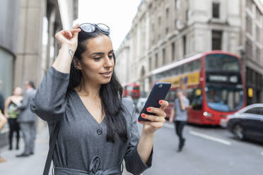 Geschäftsfrau in der Nähe einer belebten Straße, die ihr Smartphone überprüft, London, UK - WPEF01805