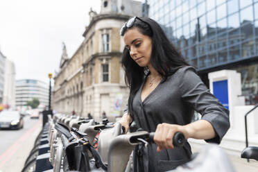 Frau in der Stadt, die ein Leihfahrrad für den Arbeitsweg benutzt, London, UK - WPEF01810