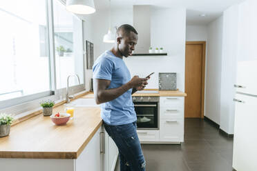 Junger Mann benutzt Mobiltelefon in der Küche zu Hause - KIJF02596
