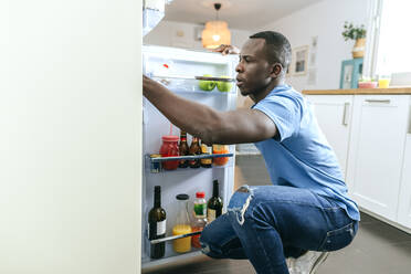 Junger Mann schaut in den Kühlschrank in der Küche zu Hause - KIJF02597