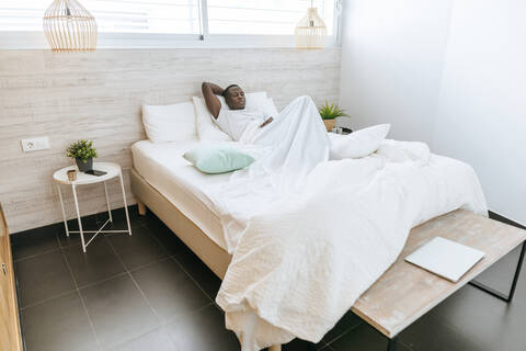 Junger Mann liegt zu Hause im Bett, lizenzfreies Stockfoto