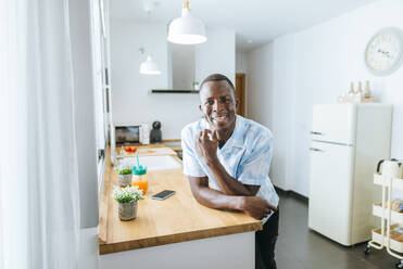 Porträt eines lächelnden jungen Mannes in der Küche zu Hause - KIJF02623