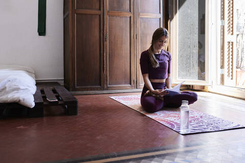 Junge brünette Frau, die im Studentenwohnheim Yoga praktiziert und ein Buch liest, lizenzfreies Stockfoto