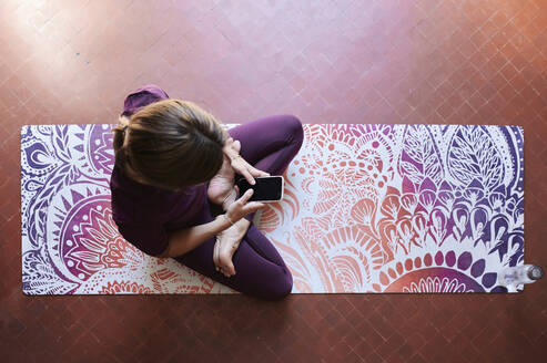 Junge brünette Frau, die Yoga praktiziert und ein Smartphone benutzt - IGGF01291