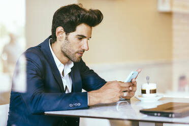 Businessman using smartphone in an urban cafe - JSMF01208