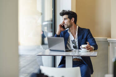 Businessman using laptop and smartphone in an urban cafe - JSMF01210