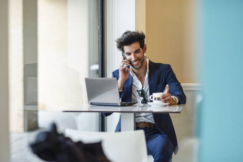 Smiling businessman using laptop and smartphone in an urban cafe stock photo