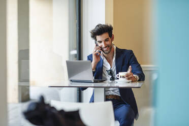 Smiling businessman using laptop and smartphone in an urban cafe - JSMF01211