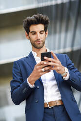 Businessman using cell phone outside an office building - JSMF01220