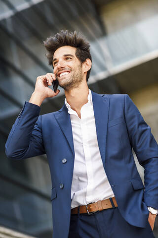 Glücklicher Geschäftsmann, der vor einem Bürogebäude mit seinem Handy telefoniert, lizenzfreies Stockfoto