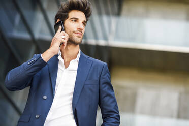 Geschäftsmann, der außerhalb eines Bürogebäudes mit einem Handy telefoniert - JSMF01223