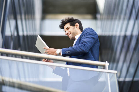 Lächelnder Geschäftsmann mit Tablet auf dem Balkon eines Bürogebäudes, lizenzfreies Stockfoto