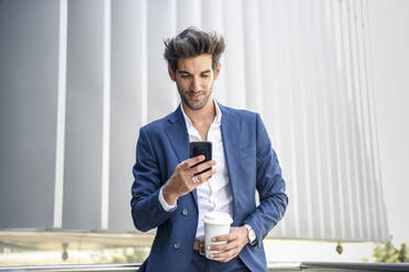 Lächelnder Geschäftsmann mit Smartphone in einer Kaffeepause im Freien - JSMF01234