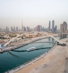 Luftaufnahme einer Yacht unter der Toleranz-Fußgängerbrücke mit den Wolkenkratzern von Dubai im Hintergrund, V.A.E. - AAEF03193