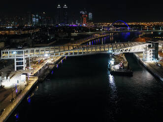 Aerial view of twisted pedestrian bridge over the Dubai Canal illuminated at night in United Arab Emirates. - AAEF03225