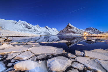 Sternspuren und Lichter auf den verschneiten Gipfeln, die sich im kalten Meer spiegeln, Volanstinden, Fredvang, Lofoten, Nordnorwegen, Skandinavien, Europa - RHPLF01194