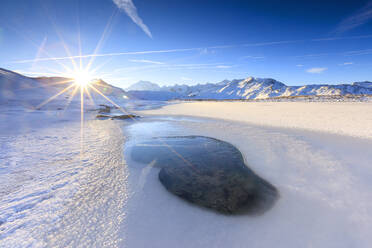 Sonnenstrahlen auf dem zugefrorenen See, Piz Umbrail umrahmt vom Monte Ortles im Hintergrund, Braulio Tal, Valtellina, Lombardei, Italien, Europa - RHPLF01203