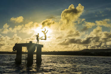 Backlit local boys jumping into the water of the lagoon of Wallis from a platform, Wallis and Futuna, Pacific - RHPLF01208