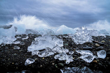 Das Wasser bricht über das Eis und den schwarzen Sandstrand von Jokulsarlon, Island, Polarregionen - RHPLF01249