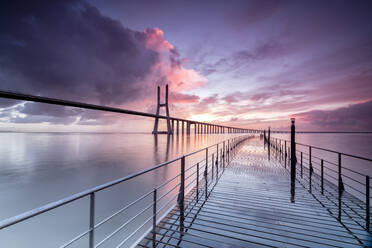 Sonnenaufgang färbt die Wolken, die sich im Fluss Tejo spiegeln und die Vasco-da-Gama-Brücke in Lissabon, Portugal, Europa einrahmen - RHPLF01387