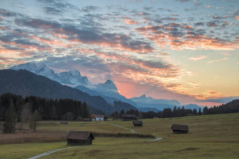 Sonnenuntergang auf Holzhütten und Wiesen mit den Alpen im Hintergrund, Geroldsee, Krun, Garmisch Partenkirchen, Oberbayern, Deutschland, Europa - RHPLF01395