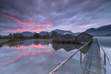 Lila Himmel bei Sonnenuntergang und Holzhütten spiegeln sich im klaren Wasser des Kochelsees, Schlehdorf, Bayern, Deutschland, Europa - RHPLF01396