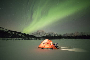 Photographer in a tent lit up by Northern Lights (aurora borealis) and starry sky in the polar night, Svensby, Lyngen Alps, Troms, Norway, Scandinavia, Europe - RHPLF01415