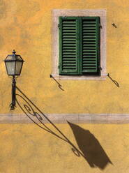 Architektonisches Detail mit grünem Holzfensterladen an gelber Wand mit verzierter Wandlampe und Schatten, San Quirico d'Orcia, Toskana, Italien, Europa - RHPLF01527