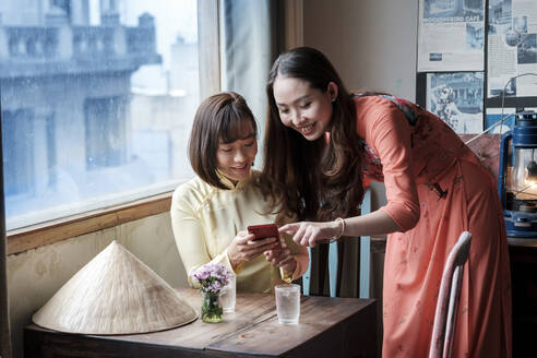 Zwei Freunde in Ao Dai-Kleidern trinken Kaffee in einem Saigoner Kaffeehaus, Ho-Chi-Minh-Stadt, Vietnam, Indochina, Südostasien, Asien - RHPLF01623