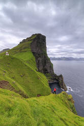 Wanderer auf den Klippen mit Blick auf den Leuchtturm von Kallur, Insel Kalsoy, Färöer Inseln, Dänemark, Europa - RHPLF01628