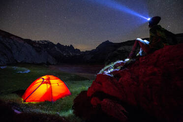 A person looks at stars near his red tent, Unterer Segnesboden, Flims, District of Imboden, Canton of Grisons (Graubunden), Switzerland, Europe - RHPLF01701