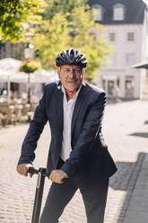 Portrait of smiling senior man with e-scooter in the city - GUSF02373