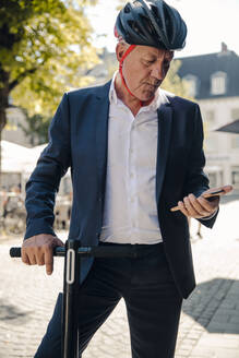 Älterer Mann mit E-Scooter in der Stadt und Smartphone - GUSF02374