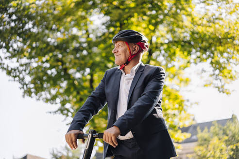 Porträt eines lächelnden älteren Mannes mit E-Roller in der Stadt - GUSF02379