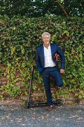 Senior man with e-scooter leaning against a wall - GUSF02383