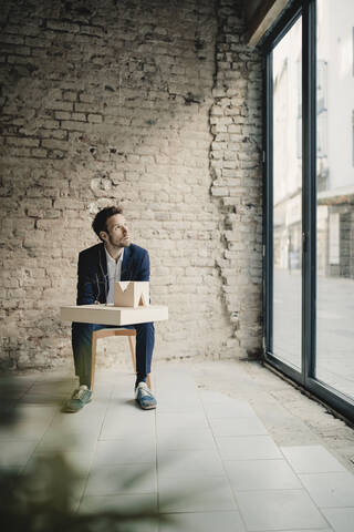 Geschäftsmann sitzt an einer Backsteinmauer mit Architekturmodell, lizenzfreies Stockfoto