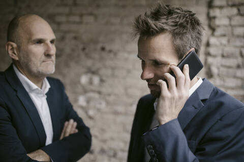 Mittelgroßer Geschäftsmann am Telefon mit einem älteren Geschäftsmann hinter ihm, lizenzfreies Stockfoto