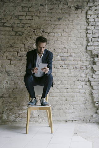 Geschäftsmann sitzt auf einem Stuhl und benutzt ein Tablet, lizenzfreies Stockfoto