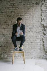 Businessman sitting on chair using tablet - GUSF02456