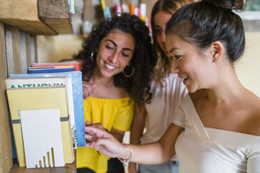 Three smiling young women at a bookshelf - MGIF00664