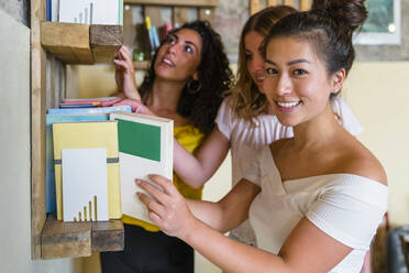 Three smiling young women at a bookshelf - MGIF00665
