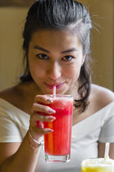 Porträt einer lächelnden jungen Frau, die einen Smoothie trinkt - MGIF00672