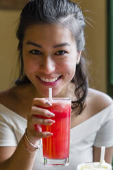 Porträt einer lächelnden jungen Frau, die einen Smoothie trinkt - MGIF00674