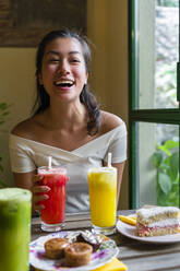 Lachende junge Frau trinkt einen Smoothie in einem Café - MGIF00675