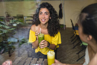 Porträt einer lächelnden jungen Frau mit einem gesunden Getränk in einem Bistro - MGIF00676