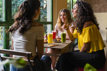 Three happy young women with smoothies meeting in a cafe - MGIF00677