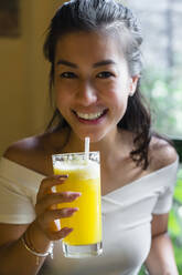 Portrait of smiling young woman drinking a smoothie - MGIF00680