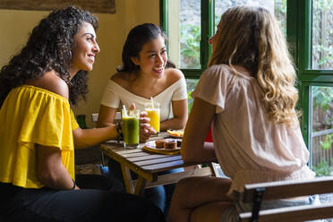 Drei glückliche junge Frauen mit Smoothies treffen sich in einem Café - MGIF00683