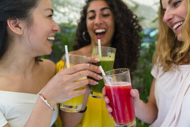 Drei glückliche junge Frauen stoßen mit gesunden Getränken an - MGIF00686